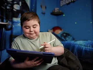 Brantley reading on a tablet while sitting on his bed