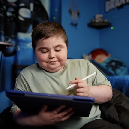 Brantley reading on a tablet while sitting on his bed