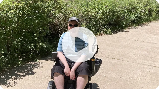 Video thumbnail: Colin seated outdoors on a paved path. Watch Colin's story.