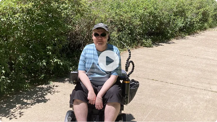 Video thumbnail: Colin seated outdoors on a paved path. Watch Colin's story.